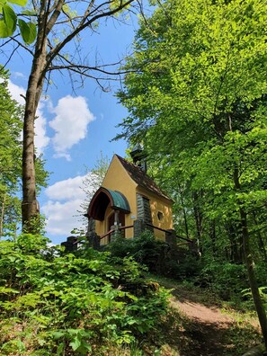 A small, yellow building with a green roof, surrounded by lush greenery and trees. - Gasthof Zur Post (Königstein)