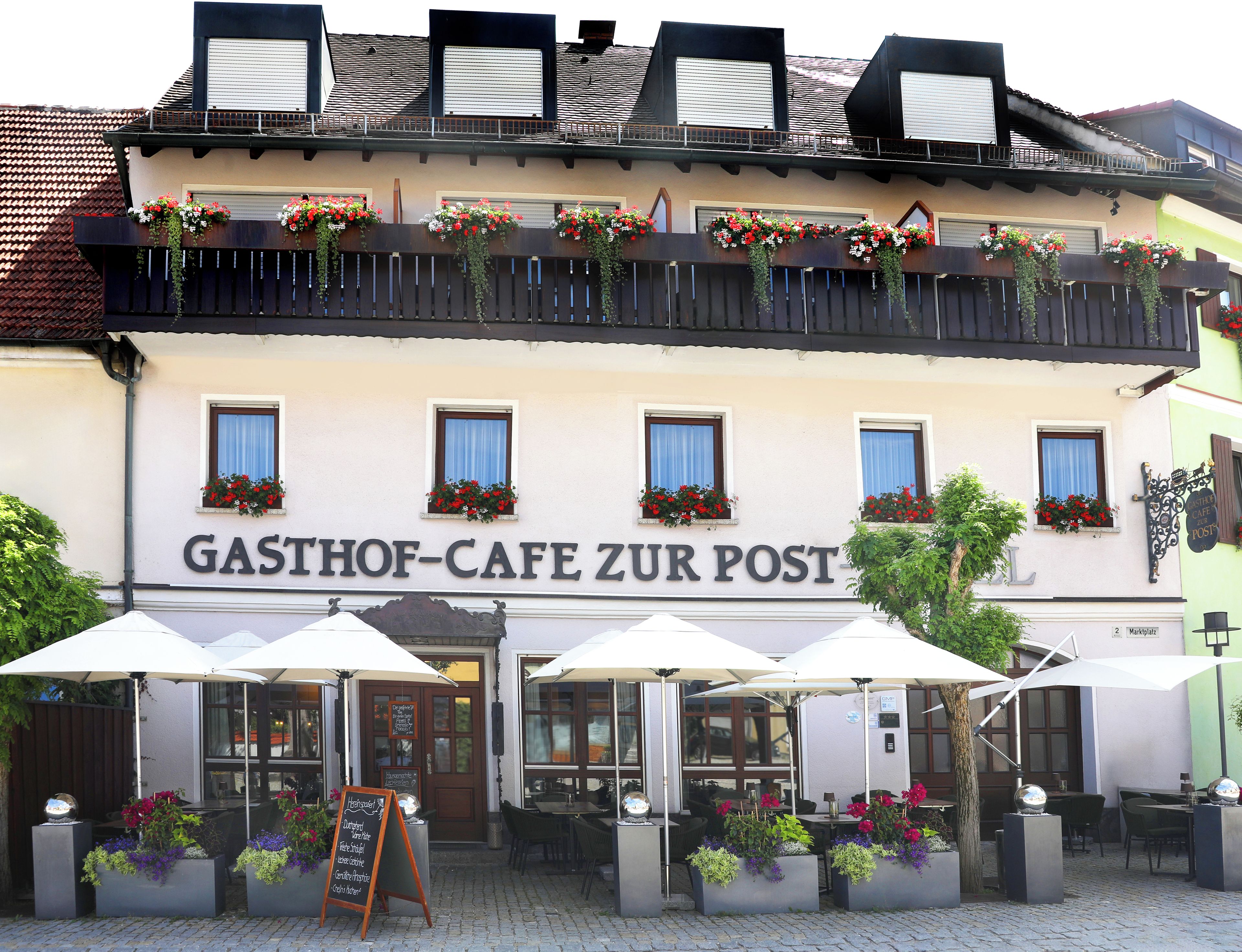 Un edificio con un letrero que dice "GASTHOF-CAFE ZUR POST" y mesas al aire libre con sombrillas.