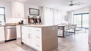 A modern kitchen with white cabinetry, a built-in island, and a dining area with a table and chairs. - Beach Oasis  w/ screened in porch, incl beach gear, 15min walk to beach (Naples)