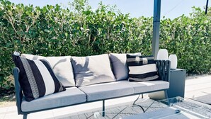 A modern outdoor seating area with a grey sofa, patterned cushions, and a glass table with a power outlet. - Beach Oasis  w/ screened in porch, incl beach gear, 15min walk to beach (Naples)