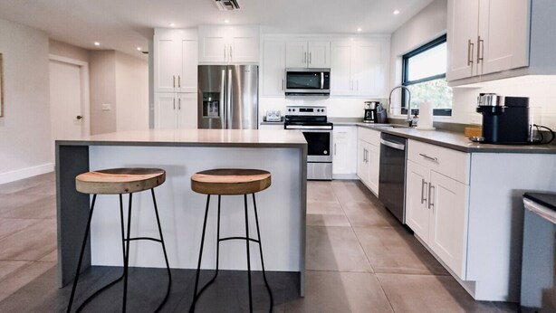 A modern kitchen with white cabinets, stainless steel appliances, and a central island with stools. - Beach Oasis  w/ screened in porch, incl beach gear, 15min walk to beach (Naples)