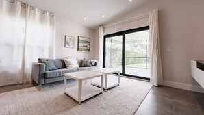 A modern living room with a grey sofa, white coffee table, and large windows with curtains. - Beach Oasis  w/ screened in porch, incl beach gear, 15min walk to beach (Naples)