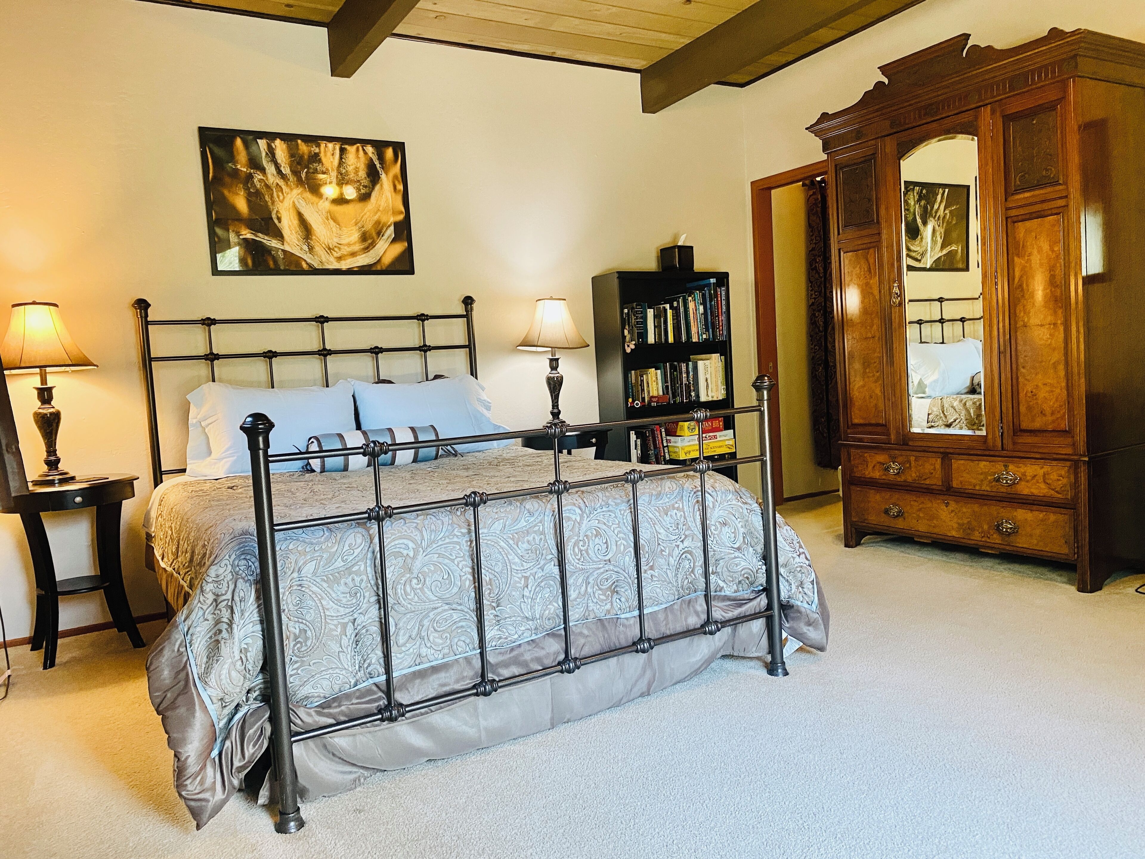 Een slaapkamer met een bed met metalen frame, een houten garderobe, een boekenplank en een schilderij aan de muur.