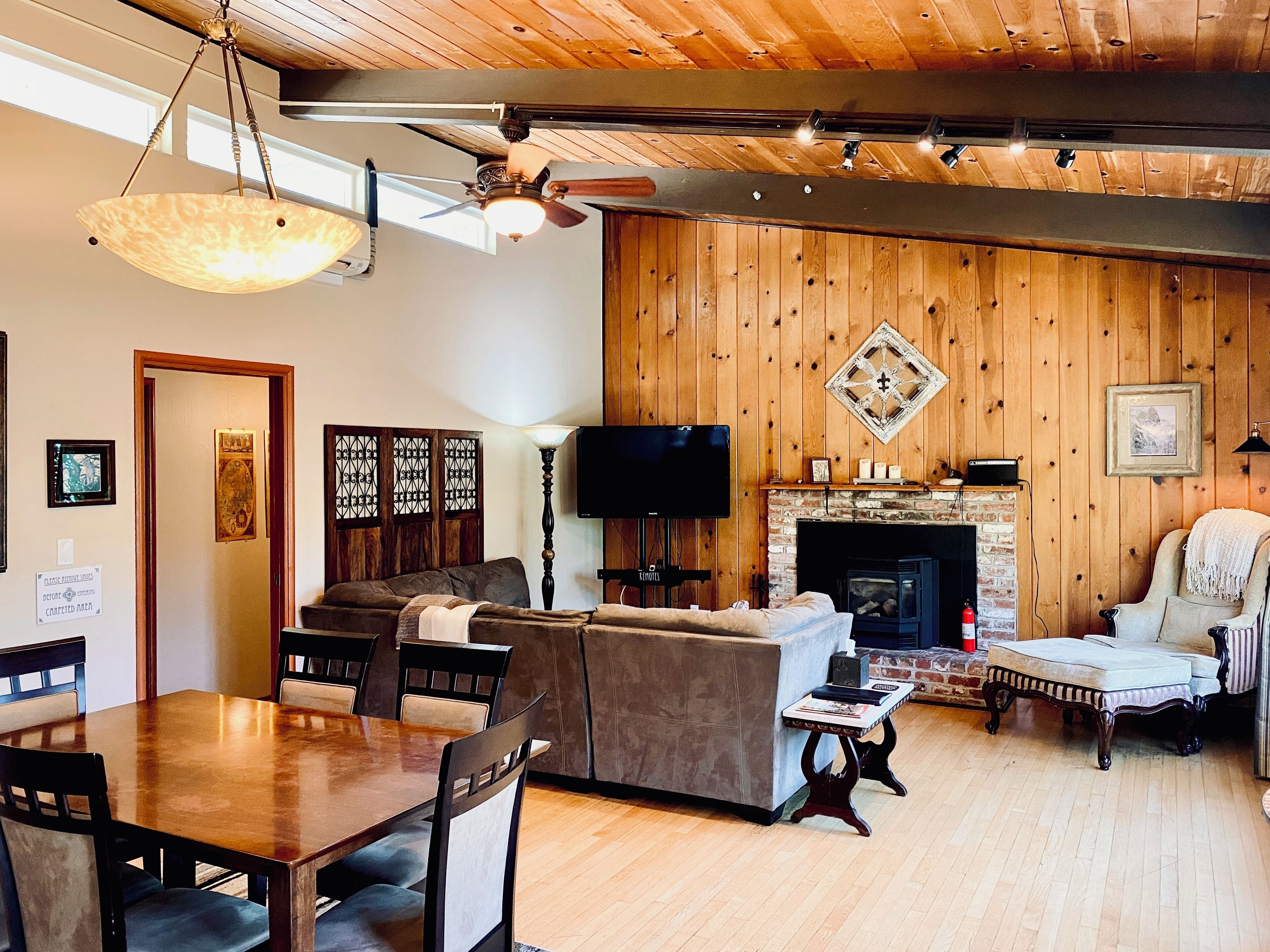 Un salon chaleureux avec une cheminée, des murs en bois, un coin repas et un téléviseur.