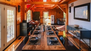A spacious dining area with a long wooden table set for a meal, wooden walls, and a high ceiling with exposed beams. - The Frontenac: A Lakeside Cabin Retreat with Sauna (Godfrey)