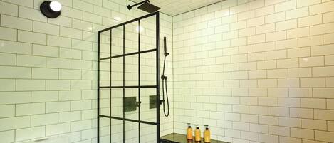 A bathroom with a white tiled wall, a black hexagonal floor, a wooden ceiling, a glass shower enclosure, and a white toilet.