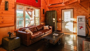 A cozy wooden cabin interior with a sofa, a coffee table, and a flag on the wall. - The Frontenac: A Lakeside Cabin Retreat with Sauna (Godfrey)