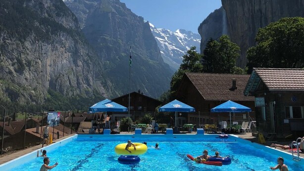 A swimming pool with people, surrounded by mountains and a clear sky.