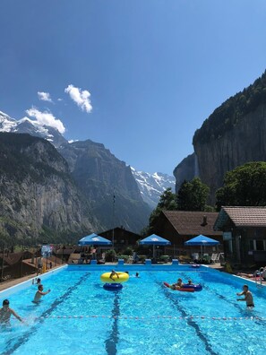 Une piscine où se baignent des gens, entourée de montagnes et sous un ciel dégagé.