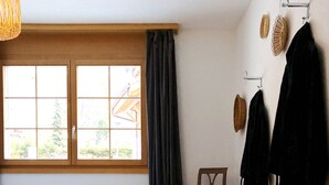 A bedroom with a bed, a chair, a window with curtains, and a wall-mounted rack with items.