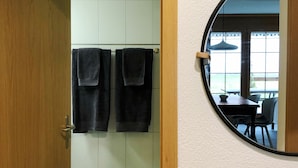 A bathroom with a wooden door, two towels hanging on a rack, and a round mirror on the wall.