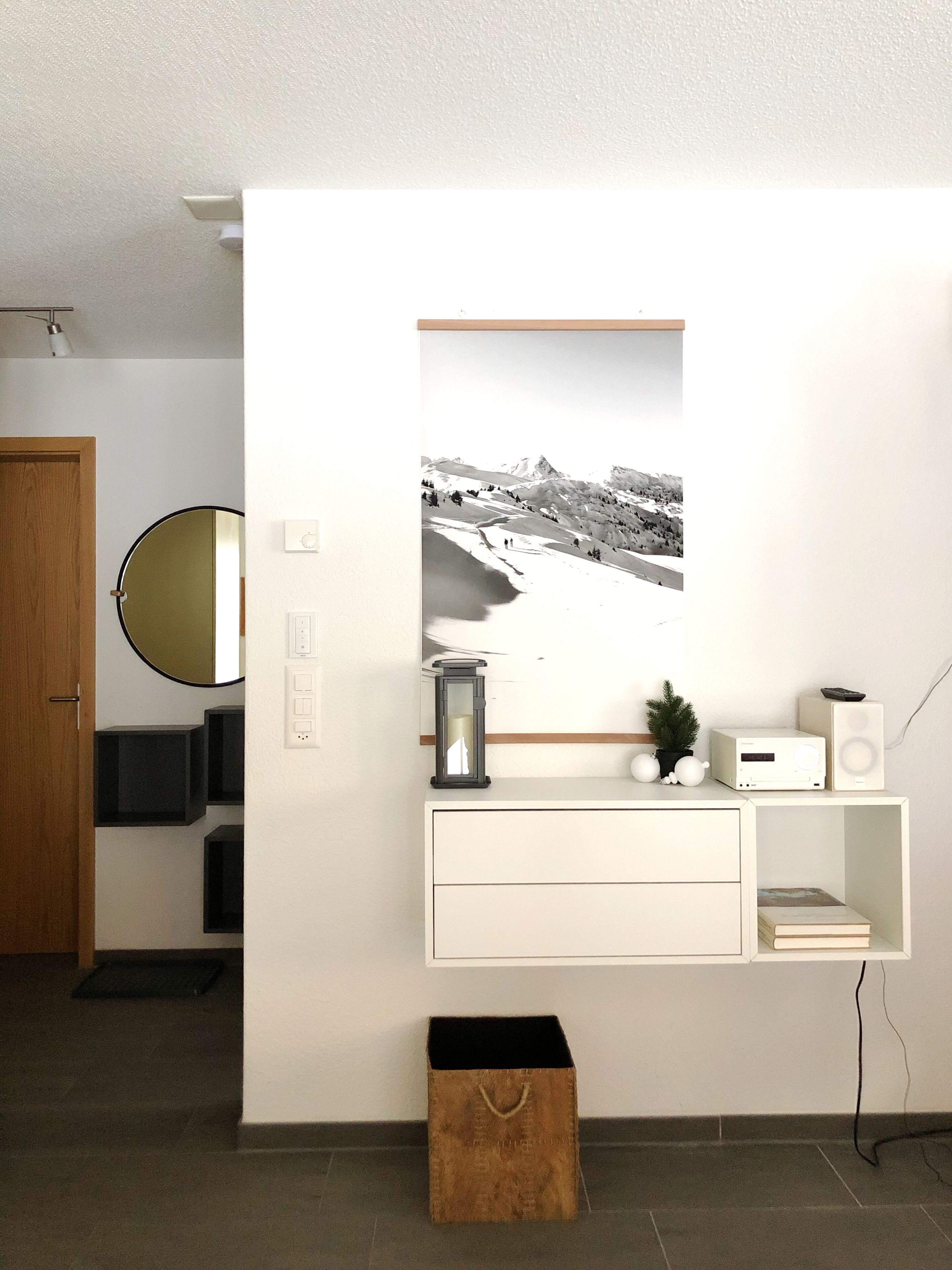 Un salon moderne avec une console blanche, une photographie en noir et blanc encadrée, une petite plante en pot et un haut-parleur.