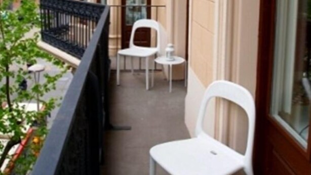A balcony with two white chairs and a small table, overlooking a street with buildings and trees. - 3BR/3BA Painted in White Apartment with Balcony. Free luggage storage service. (Barcelona)