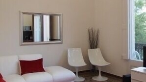 A modern living room with a white sofa, red cushions, two white chairs, a red rug, and a large window offering a view of greenery outside. - 3BR/3BA Painted in White Apartment with Balcony. Free luggage storage service. (Barcelona)