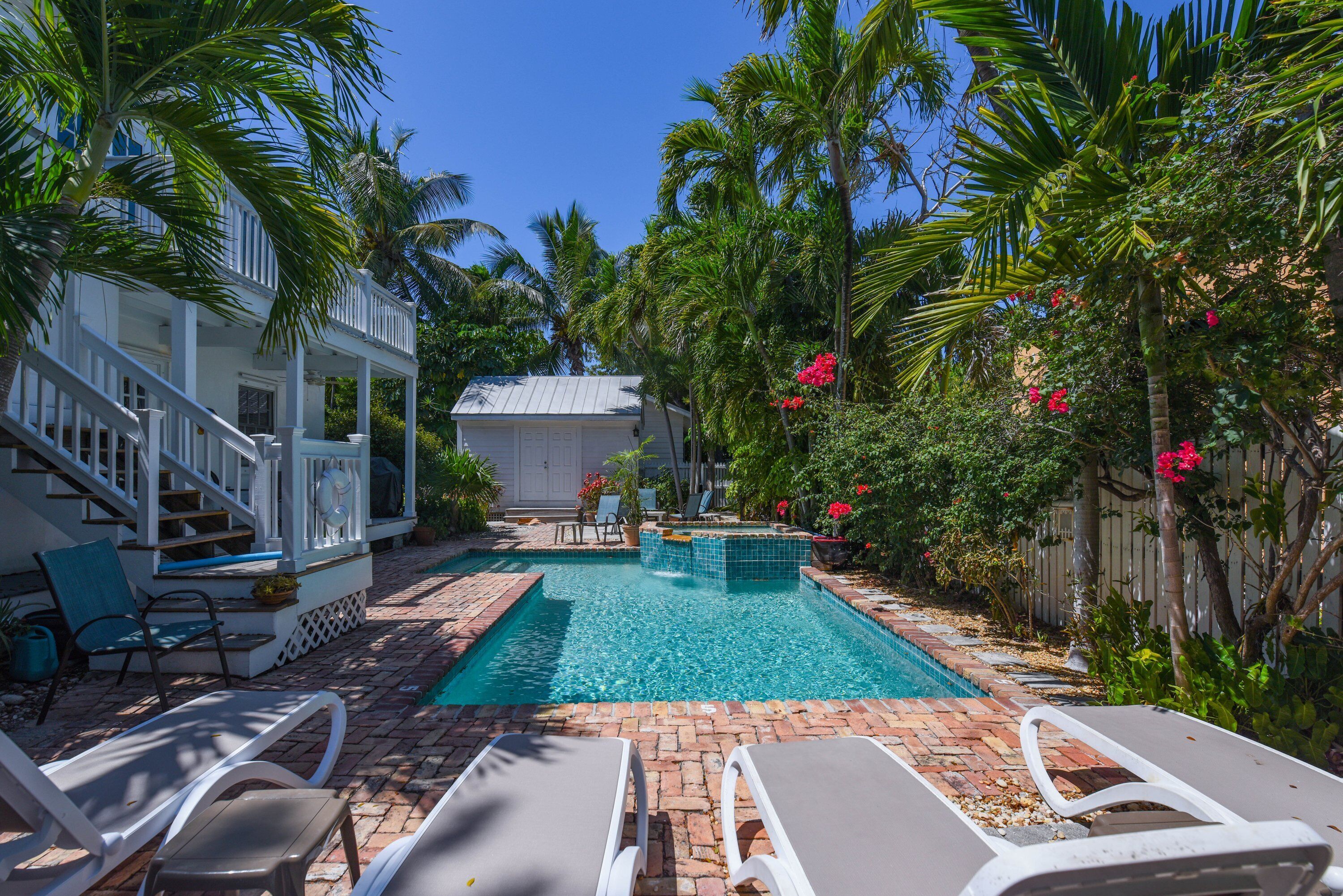 A pool area with lounge chairs, a covered deck, and a house in the background.