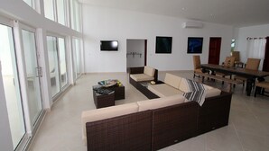 A modern living room with a large sofa, a dining table, and a TV mounted on the wall.