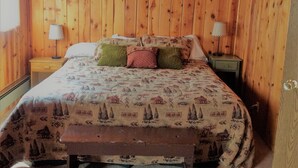 Un dormitorio con paneles de madera, una cama, dos mesitas de noche y un banco.