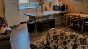 Cocina compacta con refrigerador, estufa, microondas y un pequeño comedor con una banca y sillas.