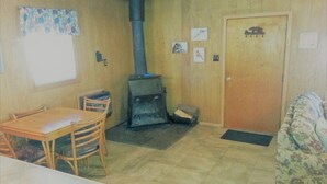 Una habitación con piso de madera, una mesa con sillas, un sofá, una chimenea y una puerta.