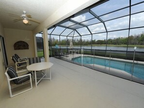 Un patio techado con piscina, zona de estar y vista al lago.