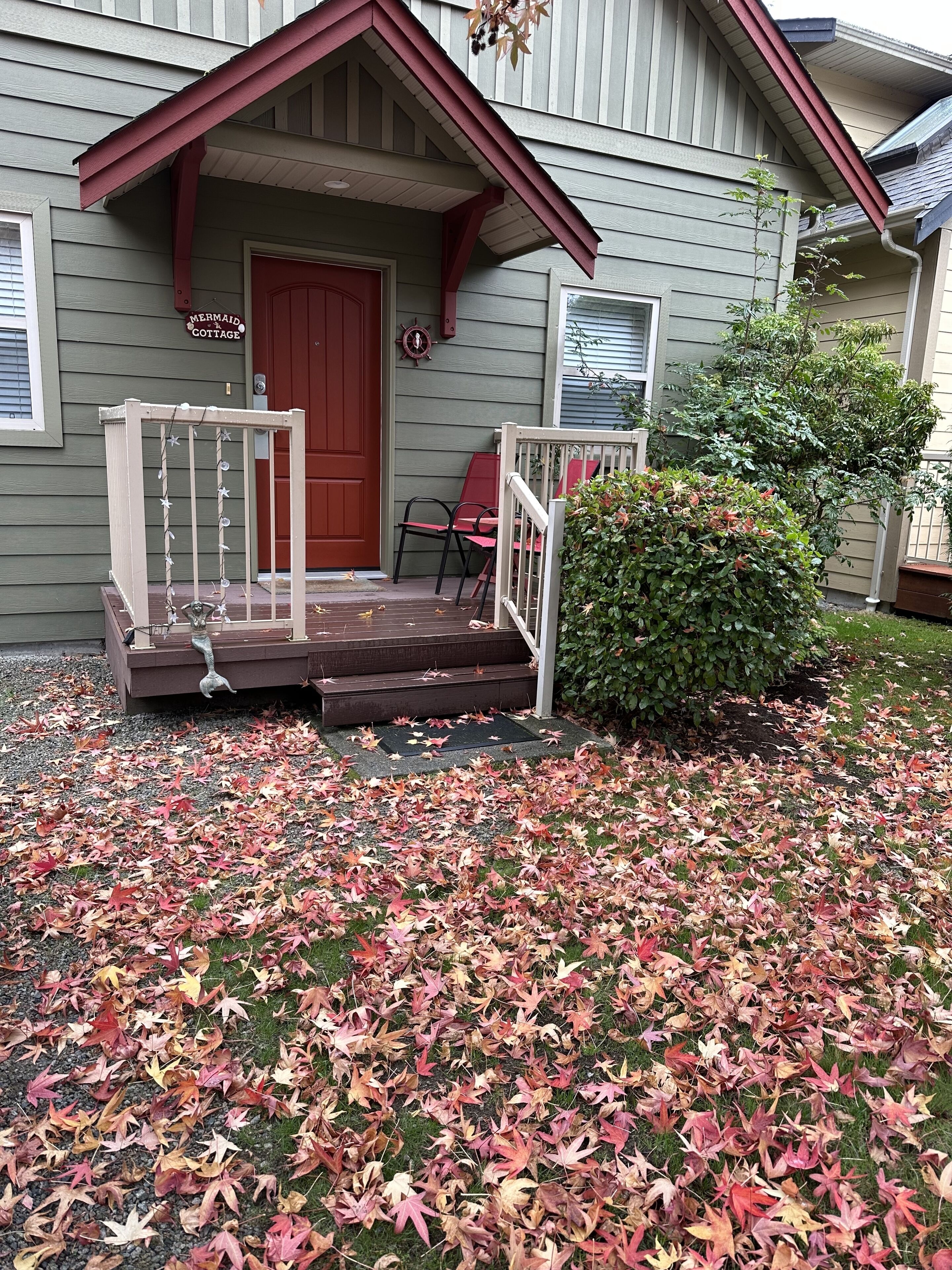 A house with a porch, a red door, and a sign that reads "Mermaid Cottage."