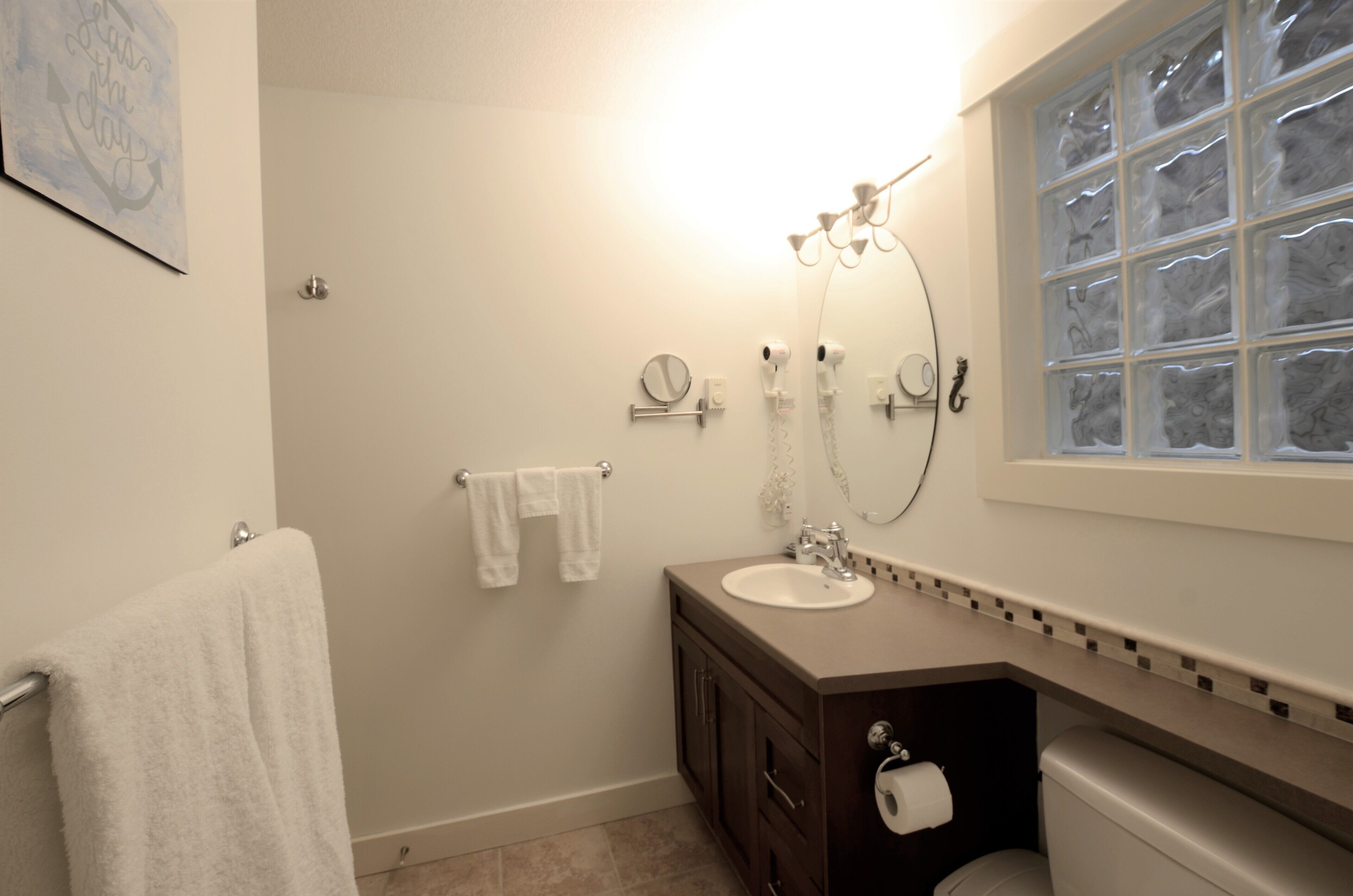 A bathroom with a sink, mirror, towel rack, and a window with frosted glass.