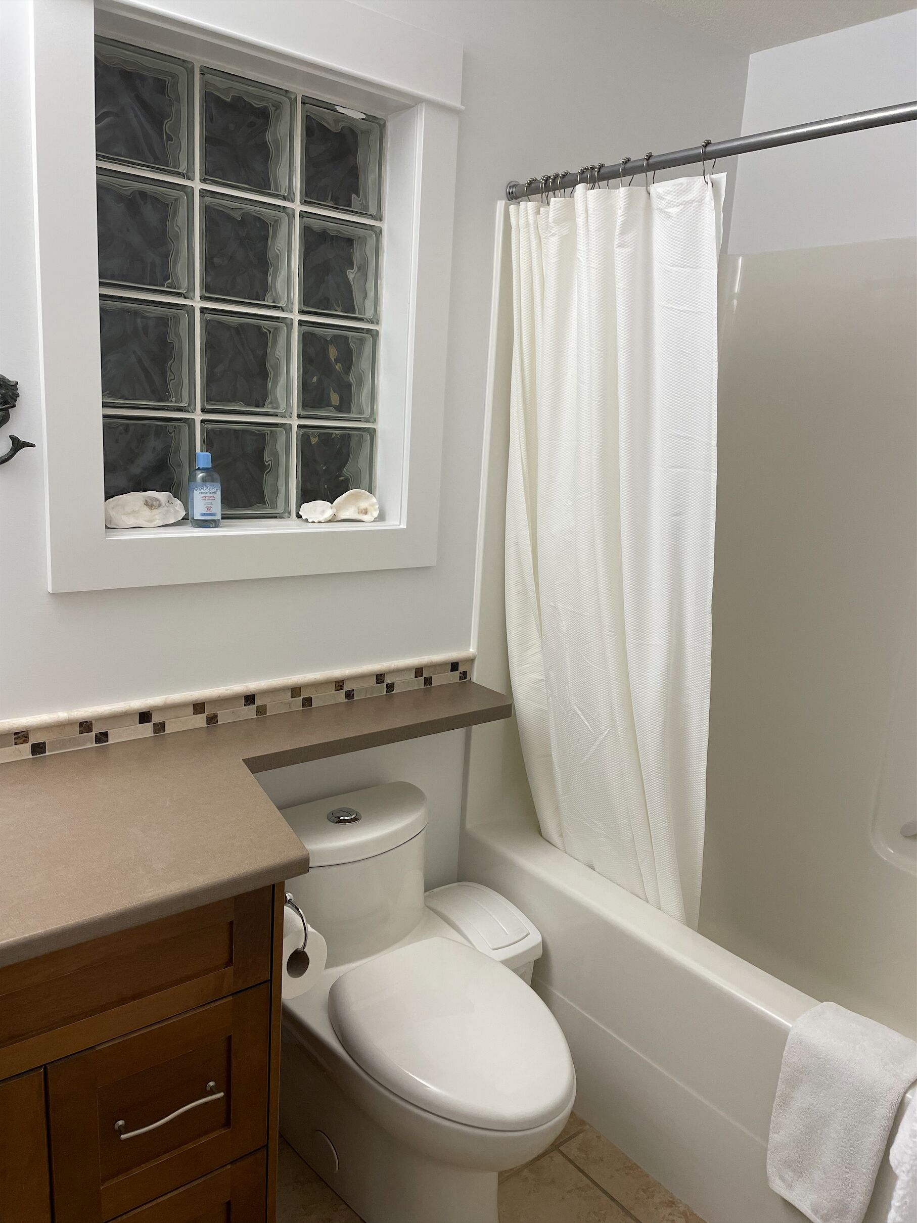 A bathroom with a toilet, a bathtub, a shower curtain, and a window with decorative tiles.