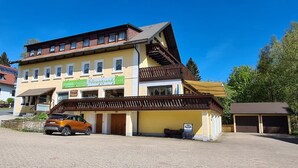 A two-story building with a yellow facade, a sign for 'Wiesengrund Pension', and a parked car in front. - Verwöhn-Pension Wiesengrund (Bischofsgruen)
