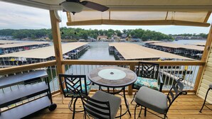 A covered outdoor deck with a table and chairs, overlooking a marina with boats and docks. -  Remodeled Ledges Lakefront 2BR Condo! No Steps. Walk-In Unit w/ WiFi. (Osage Beach)