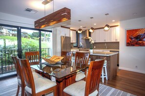 Une cuisine moderne avec une table à manger en verre, des chaises en bois et une vue sur un jardin luxuriant.