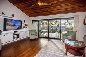 Een woonkamer met een grote televisie, houten plafond en uitzicht op het strand door de schuifglazen deuren.