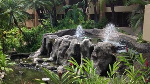 A landscaped garden with a water feature, including a cascading waterfall and a pond, surrounded by tropical plants and palm trees. - NOTHING BUT OCEAN VIEWS! Remodeled, AC, direct ocean front, large 2bd/2bth (Lahaina)