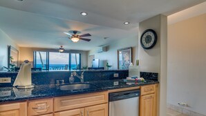 A modern kitchen with a large island, wooden cabinets, a dishwasher, and a ceiling fan. - NOTHING BUT OCEAN VIEWS! Remodeled, AC, direct ocean front, large 2bd/2bth (Lahaina)