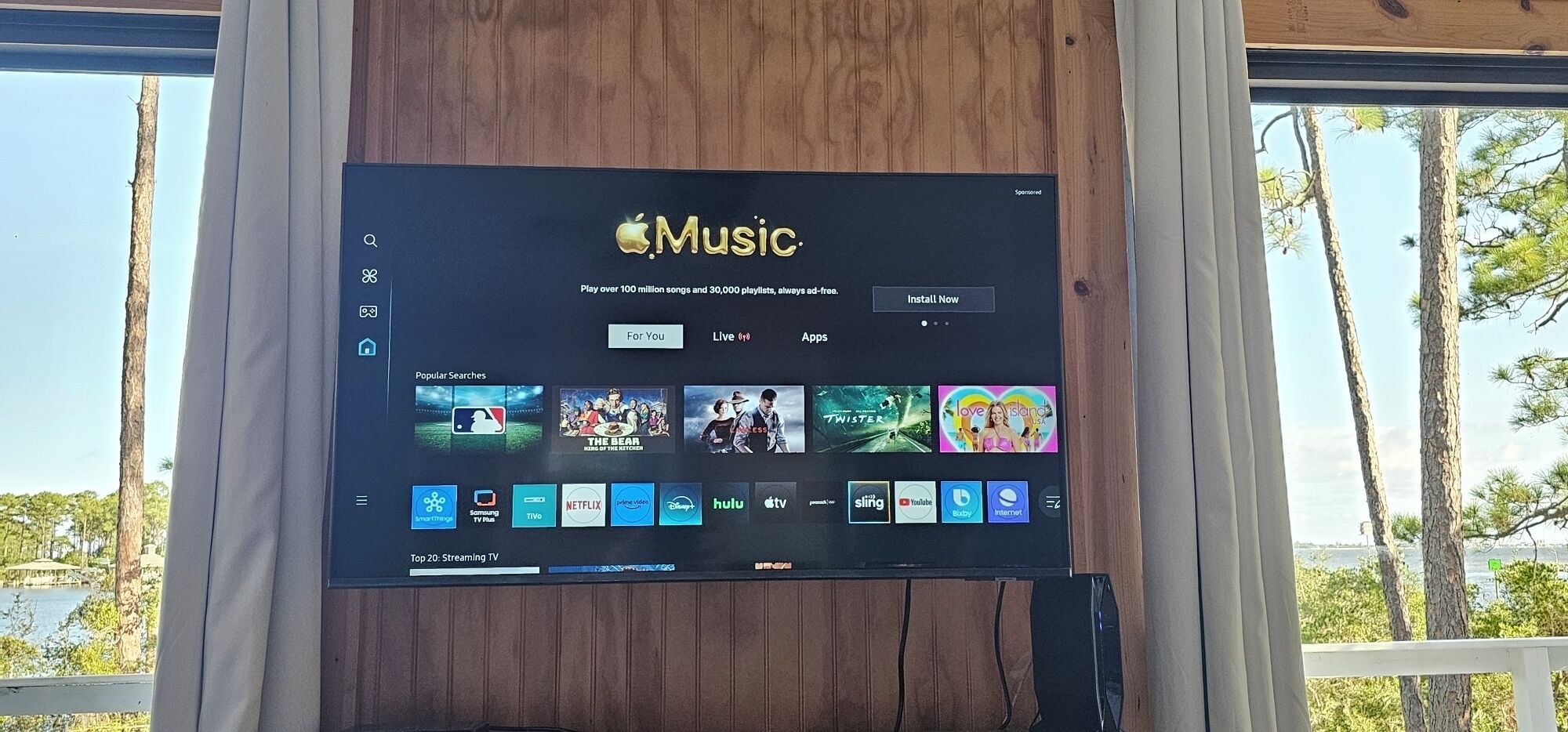An Apple Music interface on a screen with a view of trees and a body of water in the background.