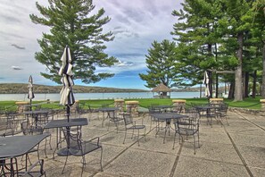 Une terrasse extérieure avec des tables et des chaises, offrant une vue sur un plan d’eau et des collines.