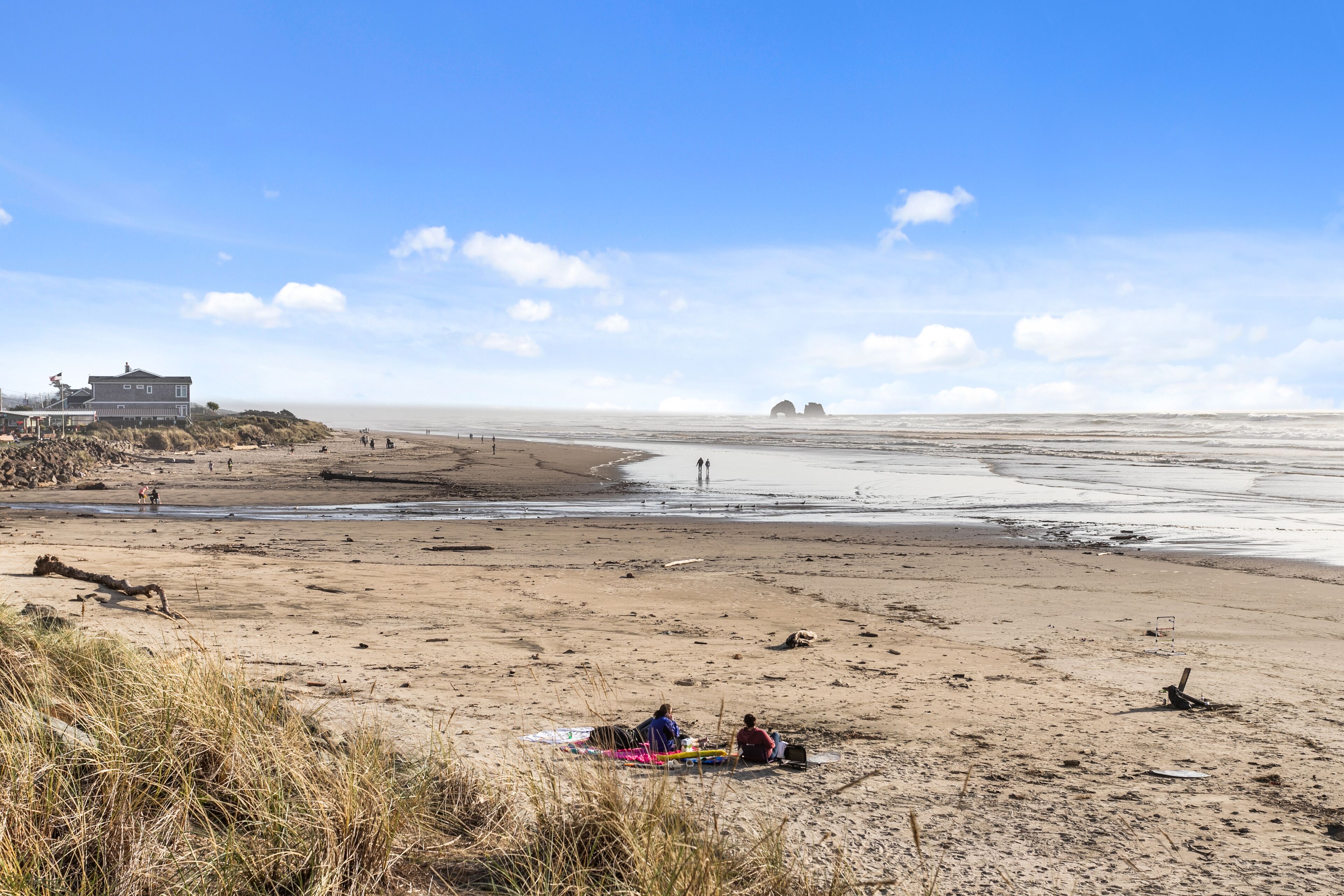 Una playa con una casa al fondo, algunas personas y un cielo despejado.