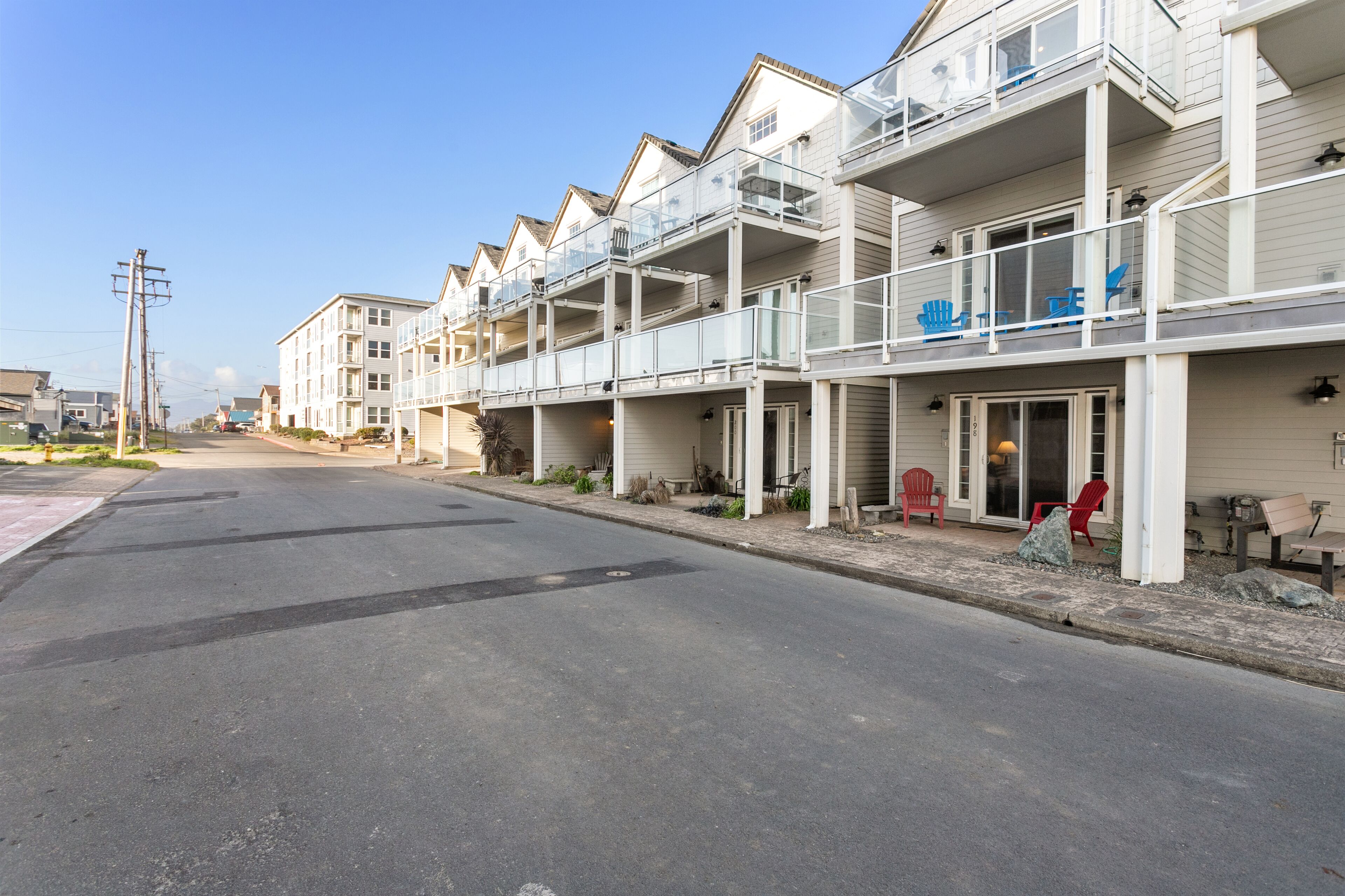 A row of beachfront condominiums with balconies, a clear sky, and a quiet street.