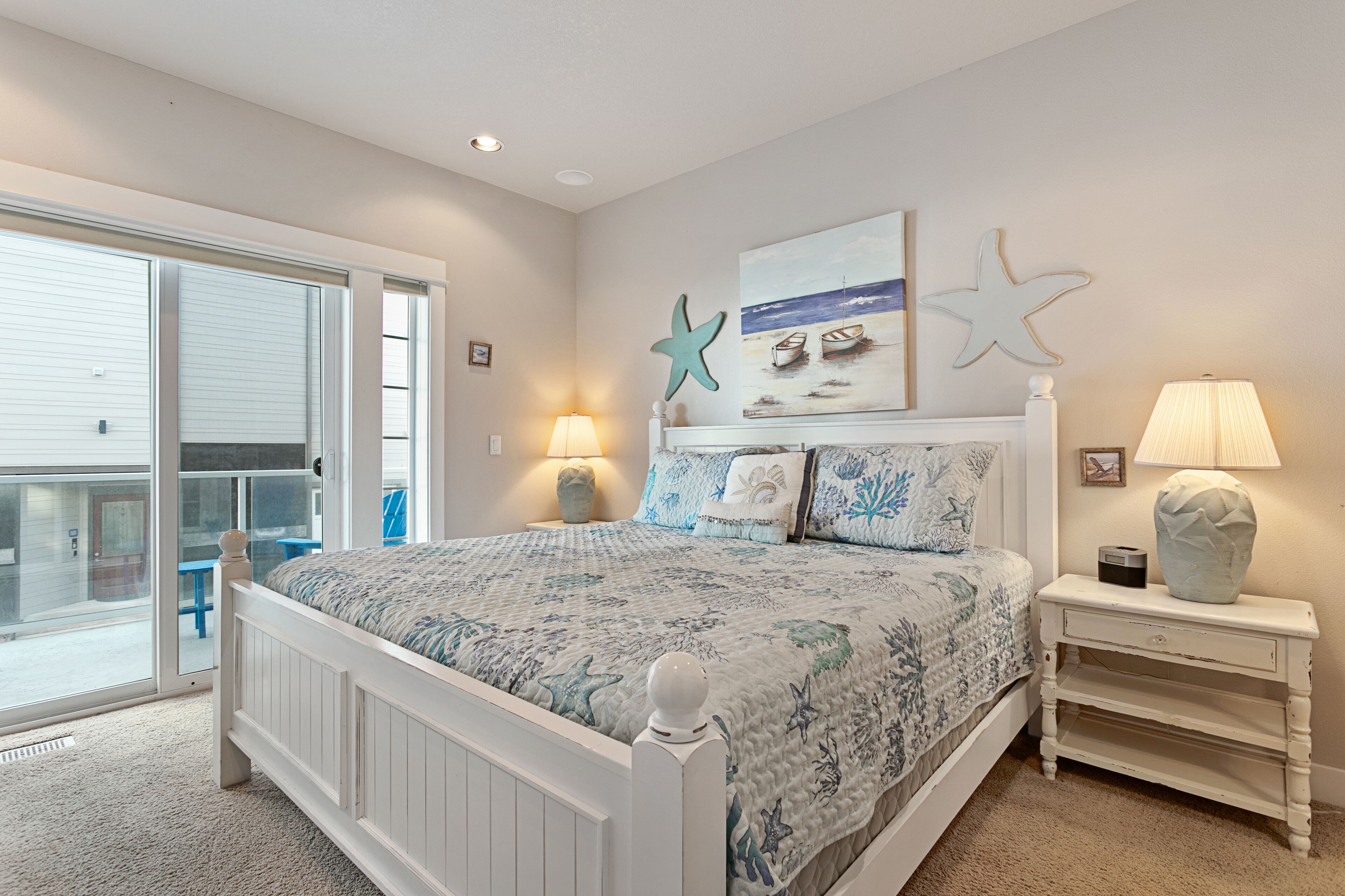 Un dormitorio con cama, mesita de noche, lámpara, decoración de estrella de mar y un cuadro de barcos en la pared.