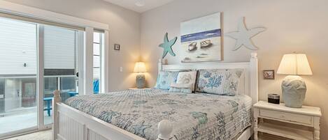 Un dormitorio con cama, mesita de noche, lámpara, decoración de estrella de mar y un cuadro de barcos en la pared.