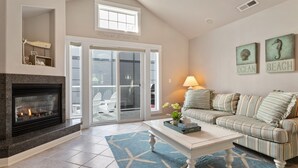 A living room with a fireplace, a sofa, a coffee table, and a view of the ocean through large sliding glass doors.