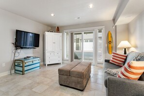 Ein Wohnzimmer mit einem Flachbildfernseher, einer Stauraumkiste, einer gepolsterten Bank, einem Sofa mit gestreiften Kissen und einem Surfbrett an der Wand.