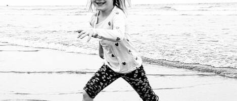 A child playing on a beach with waves in the background.