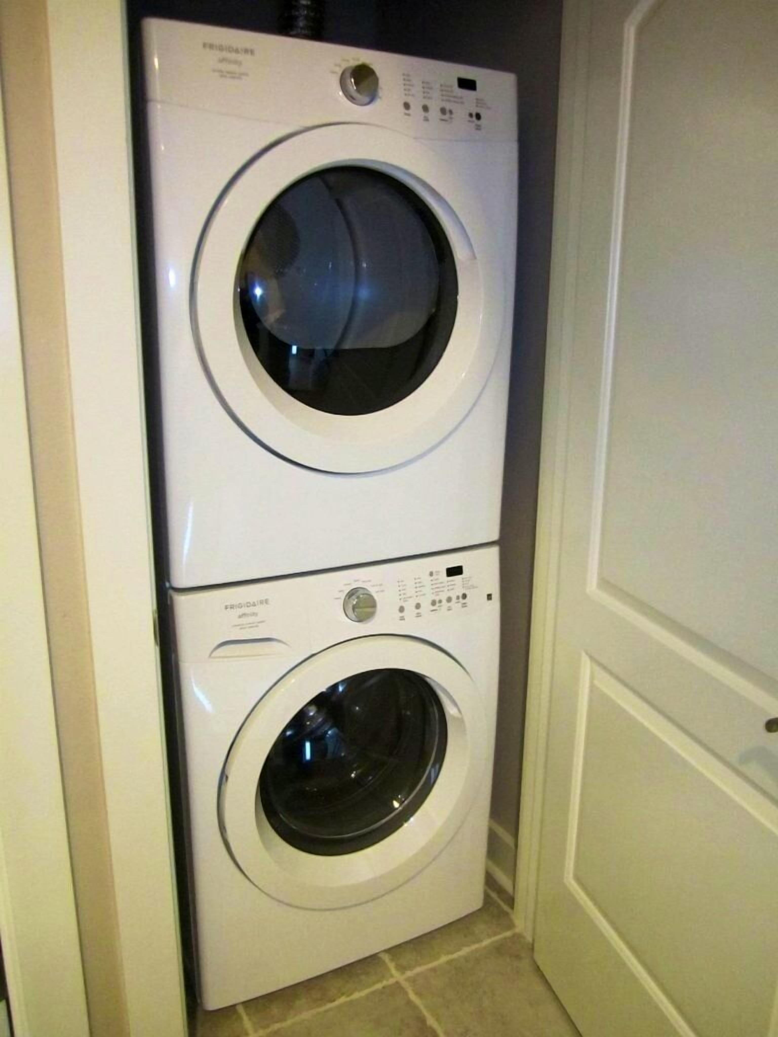 A stacked washer and dryer unit in a corner of a room.