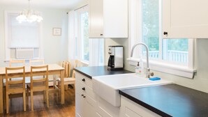 A modern kitchen with white cabinets, a black countertop, and a window with a view of greenery. - Charming Cape Cod cottage on Depot Pond & bike trail with pond access (Eastham)