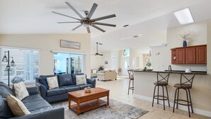 Ein geräumiges Wohnzimmer mit einem dunkelgrauen Ecksofa, einem Holztisch und einem Deckenventilator.