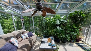 Un invernadero con ventilador de techo, un sofá con cojines estampados y varias macetas con plantas.