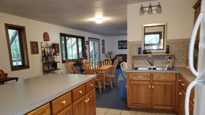 Una cocina con armarios de madera, una encimera y un refrigerador. En la zona de comedor contigua hay sillas y una mesa.