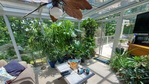 Una habitación iluminada por el sol, con ventilador de techo, sofá, mesa de centro y diversas plantas en macetas.