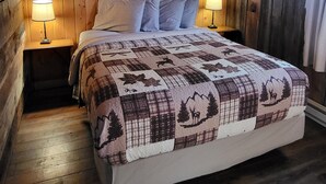 A wooden-paneled room with a bed, two bedside lamps, and a quilt with nature-themed designs. - "Elk's Run"  Rustic Cabin Hidden Among The Pines At Falls Creek. (Condon)