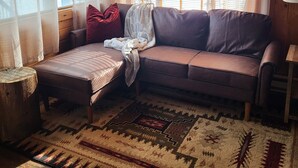 A cozy living room with a brown leather sofa, a small ottoman, and a patterned rug. - "Elk's Run"  Rustic Cabin Hidden Among The Pines At Falls Creek. (Condon)